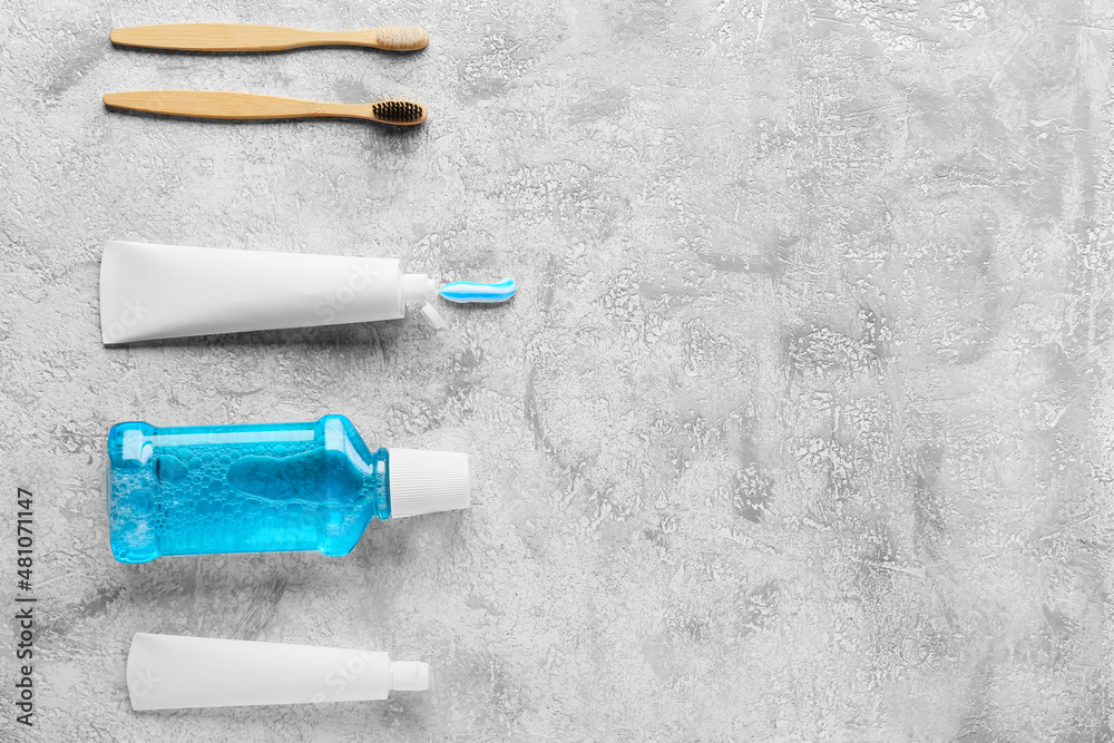 Tubes with tooth paste, brushes and mouthwash on grey background