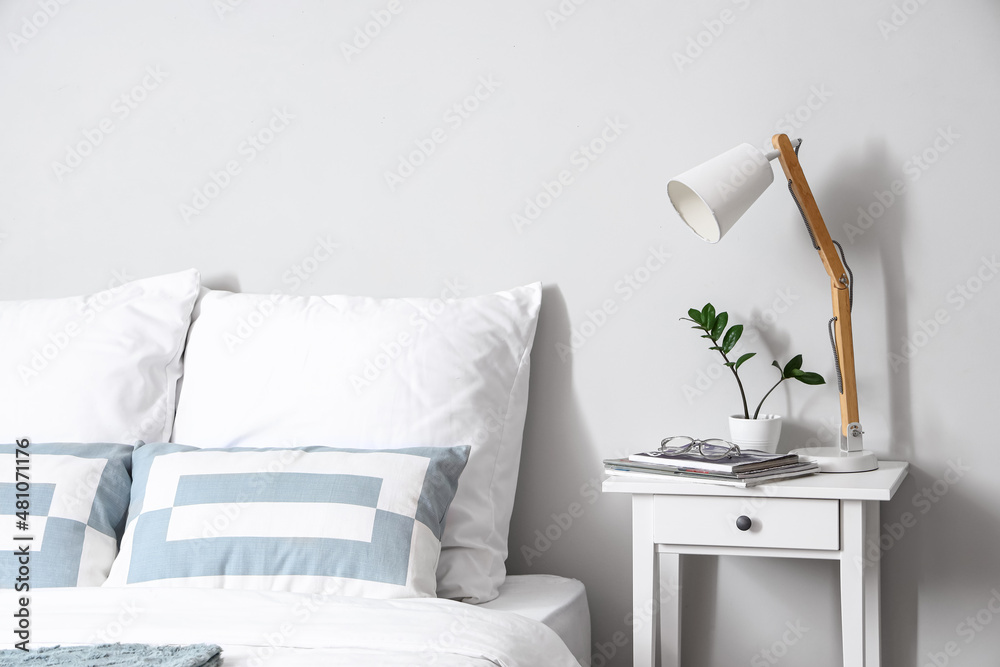 Bedside table with lamp, eyeglasses and magazines near light wall