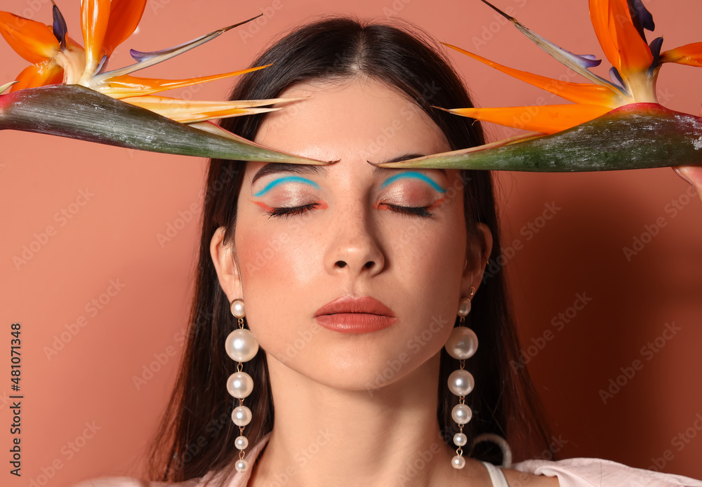 Beautiful young woman with strelitzia flowers on color background