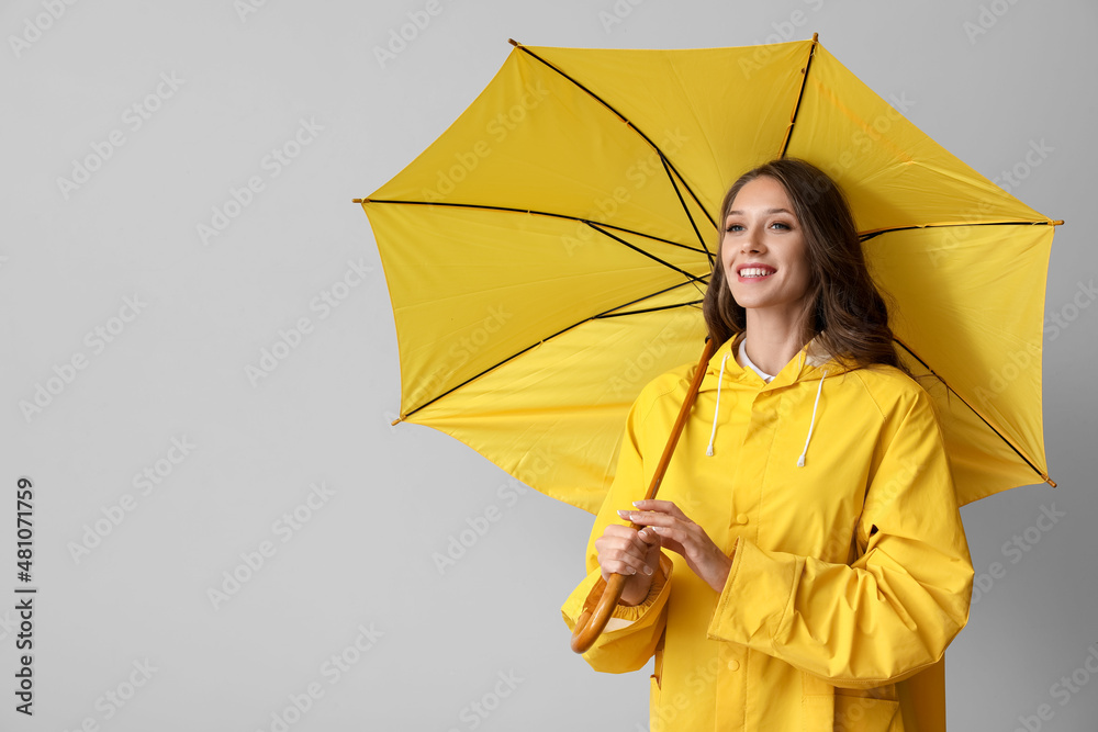 身穿黄色雨衣、灰色背景下撑开雨伞、面带微笑的美丽女人