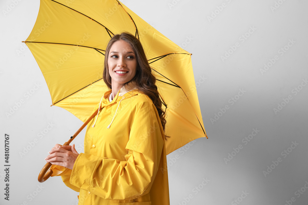 身穿黄色雨衣、灰色背景下撑开雨伞的美女