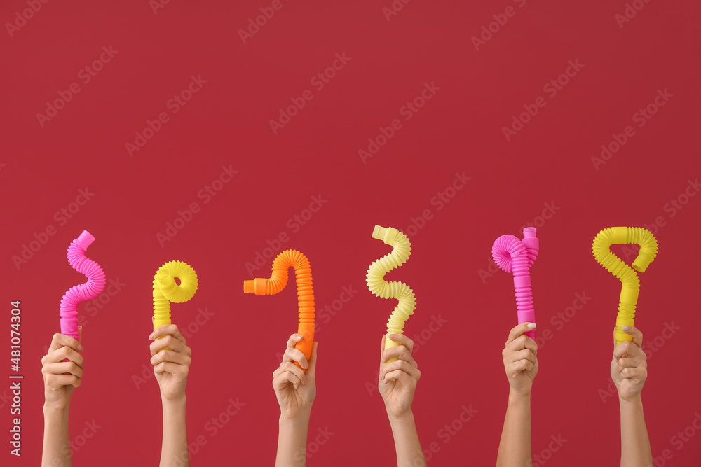 Hands with popular pop tubes on color background