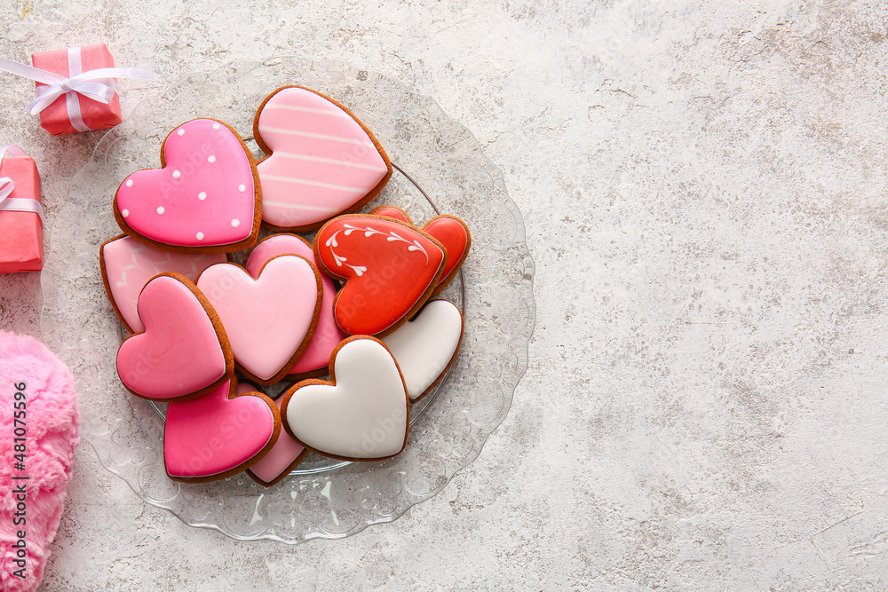 Plate with tasty heart shaped cookies and gift boxes on light background