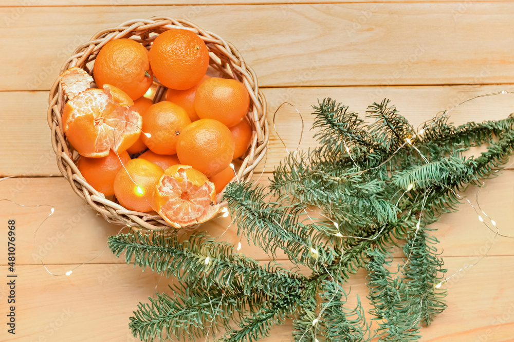 Wicker bowl with tasty tangerines, Christmas lights and fir branches on wooden background