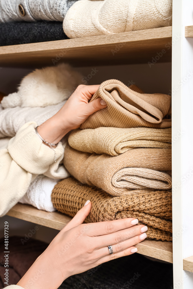 Woman taking warm sweater from shelf in wardrobe, closeup