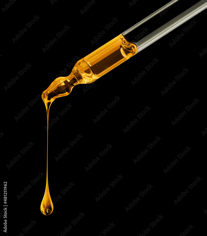 Stretched oily drop falls from a pipette close-up on a black backgroundd