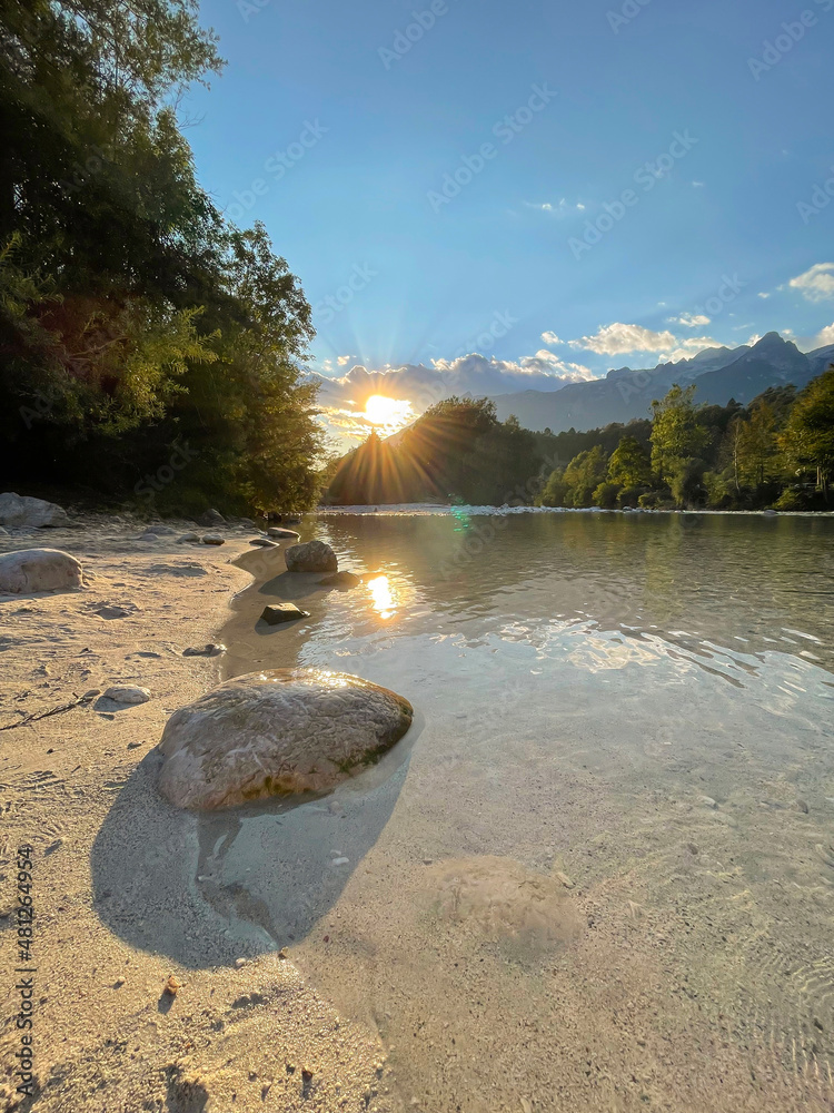 VERTICAL: Golden summer evening sunbeams shine on a sandy shore of Soca river.