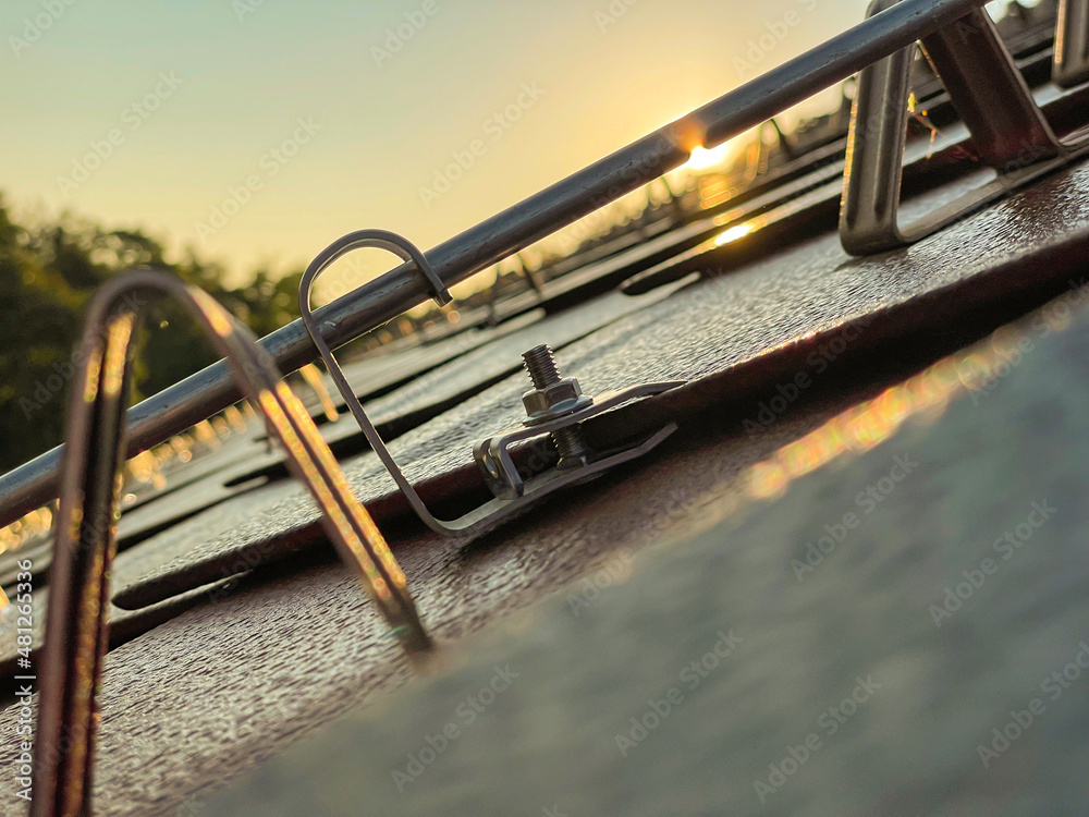 MACRO, LENS FLARE: Golden summer evening sunbeams shine on rooftop snow guards.