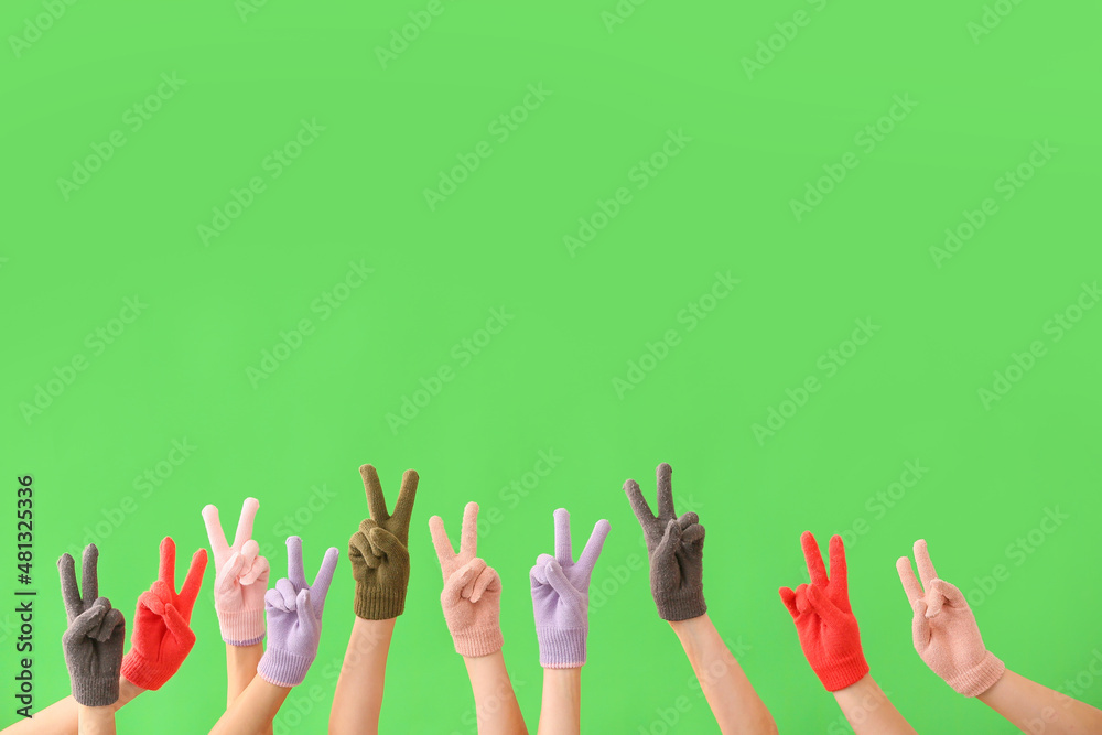 Women in warm gloves showing victory gesture on green background