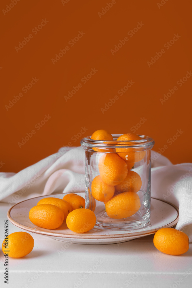 Jar with tasty kumquat fruits on light wooden table