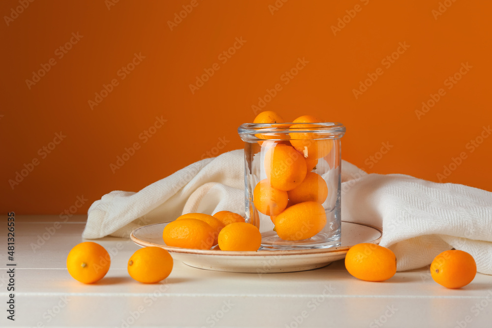 Jar with tasty kumquat fruits on table against orange wall