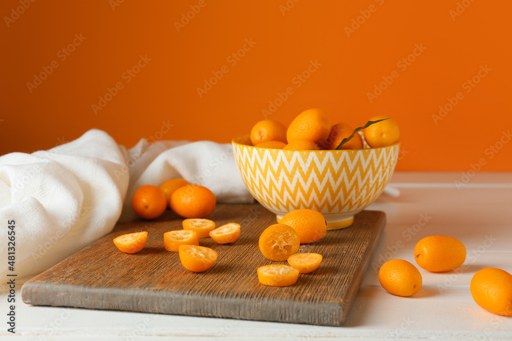 Bowl with tasty kumquat fruits on table against orange wall