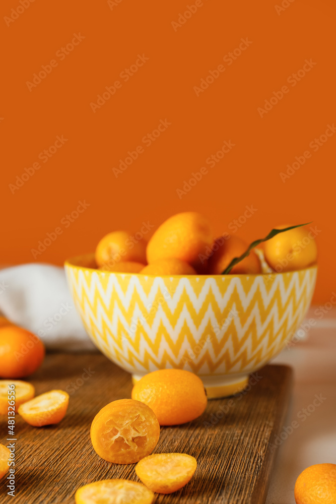 Bowl with tasty kumquat fruits on table against orange wall