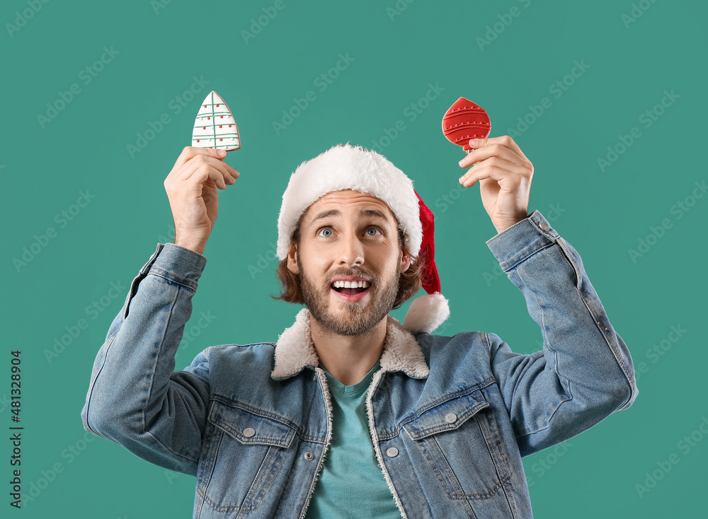 Handsome man in Santa hat with gingerbread cookies on green background