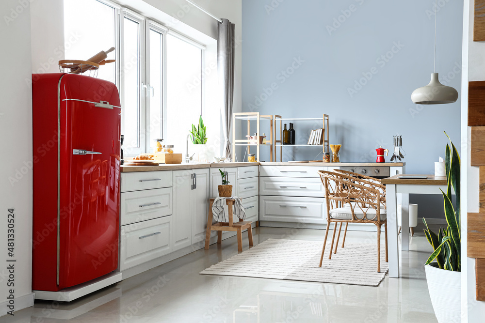 Interior of light modern kitchen with red fridge, white counters and dining table