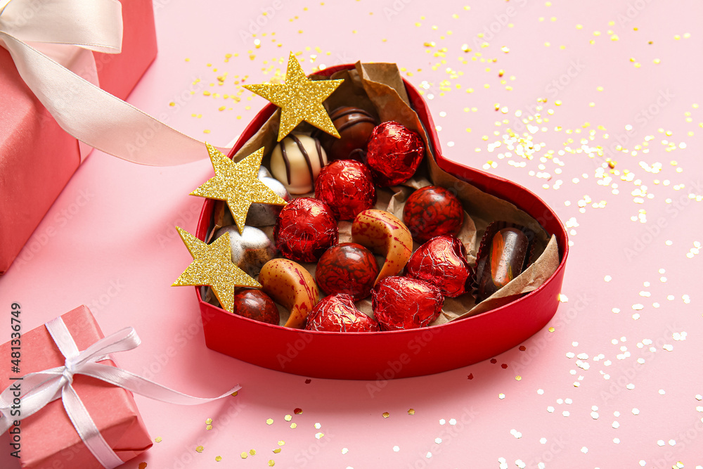 Heart shaped box with tasty chocolate candies and gifts on pink background