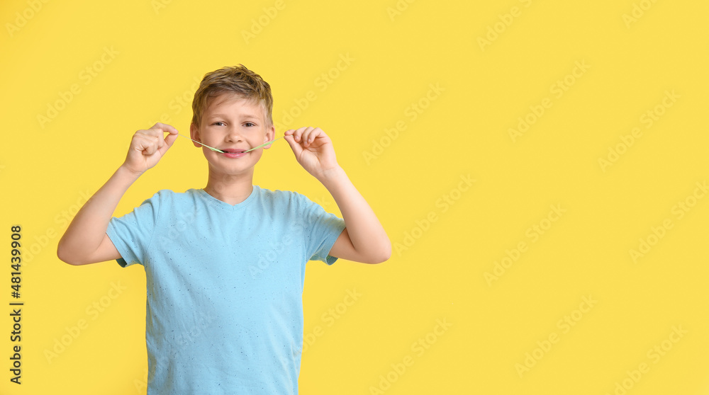 Little boy in blue t-shirt chewing gum on yellow background