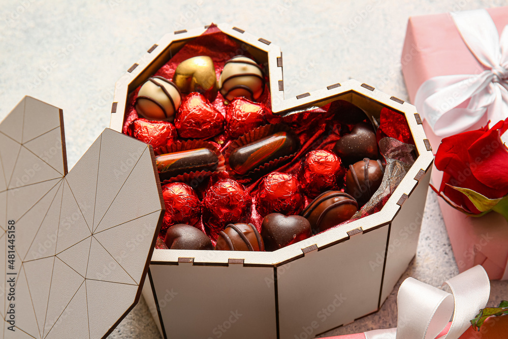 Heart shaped box with tasty chocolate candies on light background