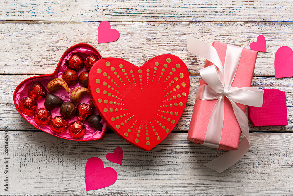 Heart shaped box with tasty chocolate candies and gift on white wooden background