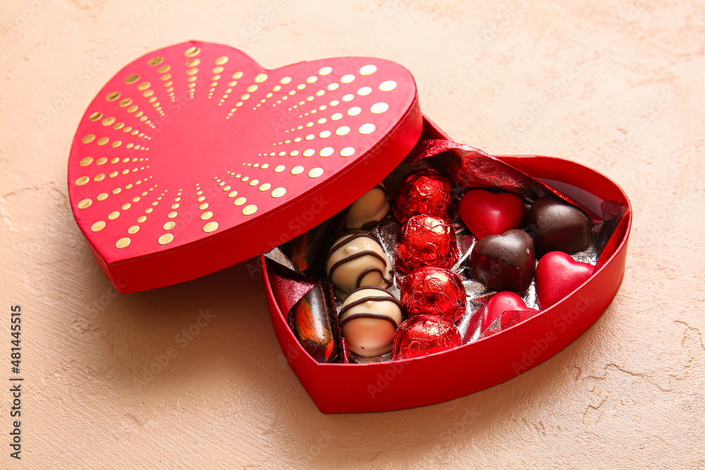 Heart shaped box with tasty chocolate candies on beige background