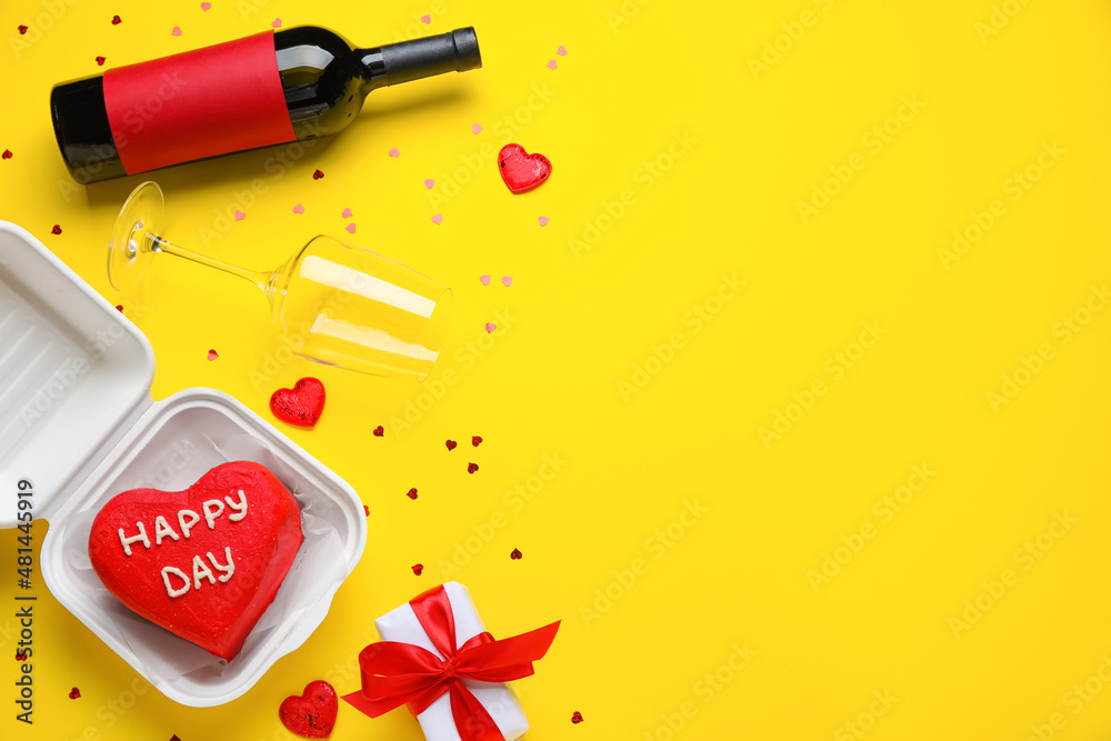 Composition with tasty bento cake, bottle of wine and gift on yellow background