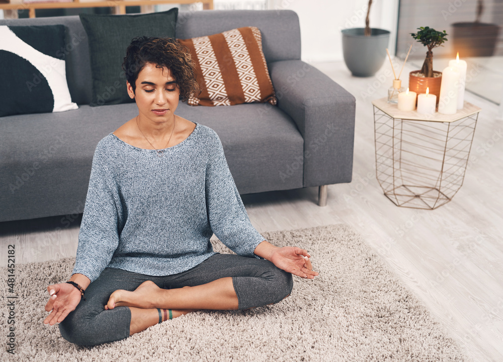 Namaste right here. Full length shot of an attractive young woman sitting and meditating in her loun