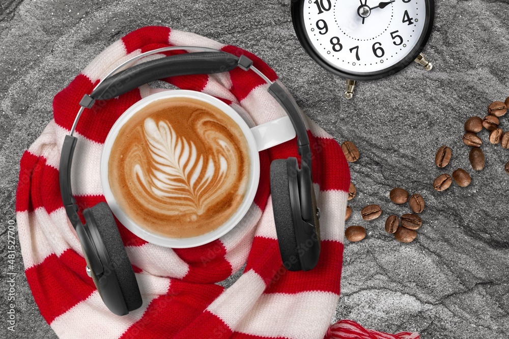 Hot coffee mug with headphones in vintage style and coffee beans on the desk.