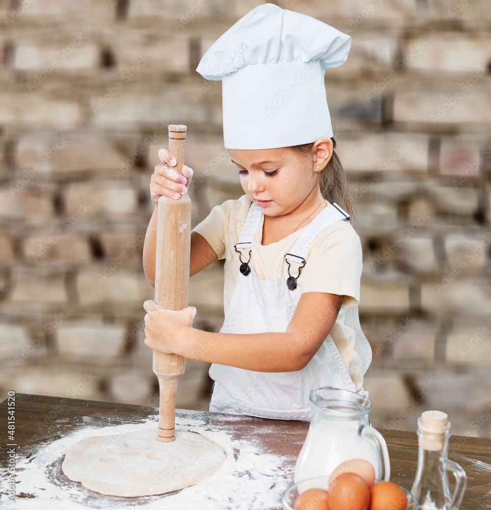 Toddler child playing with the dough in the kitchen dressed as a chef. Child baking a cake