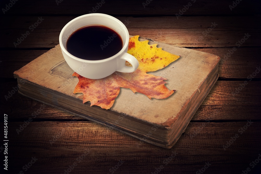 a cup of tea and a book on a wooden surface against the background of fallen leaves, autumn season