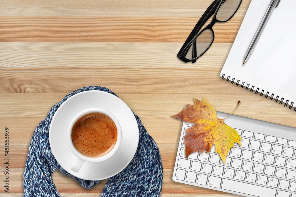 Office workspace with keyboard glasses, cup of tea and autumn leaves