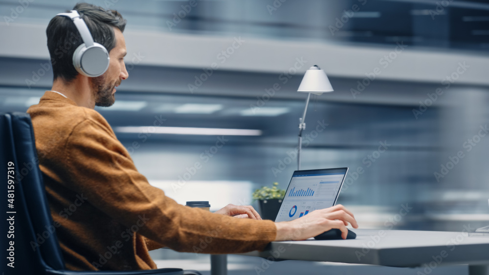 Modern Office: Handsome Businessman Sitting at His Desk Working on a Laptop Computer. Man Wearing He