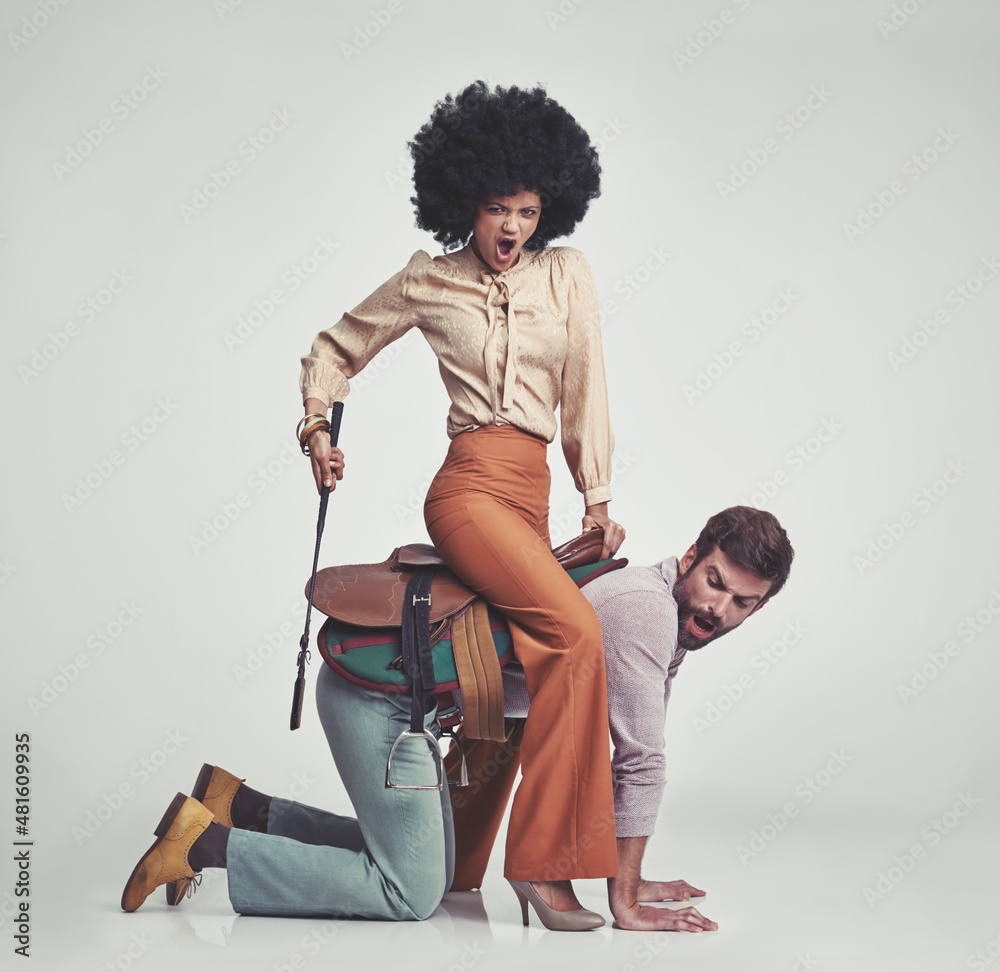 Get moving. A studio shot of an attractive woman in 70s wear riding a handsome man wearing a saddle 