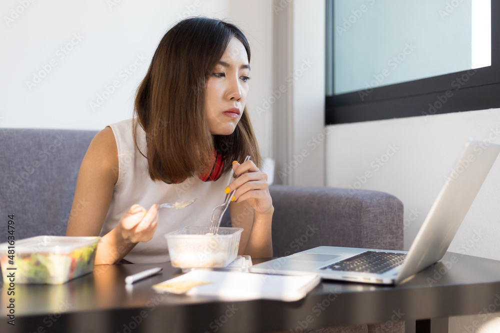 女性白天在家用笔记本电脑工作时吃午饭。在家工作和保持社交距离