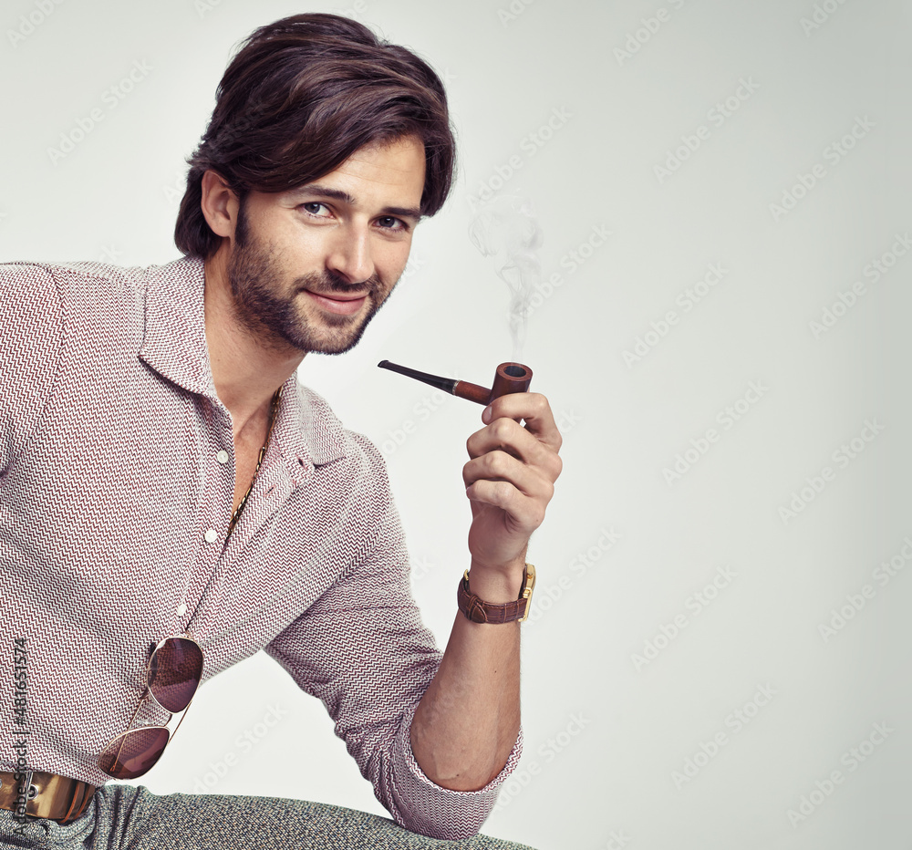 Groovy cool. A young man with 70s style sitting in the studio and smoking a pipe.