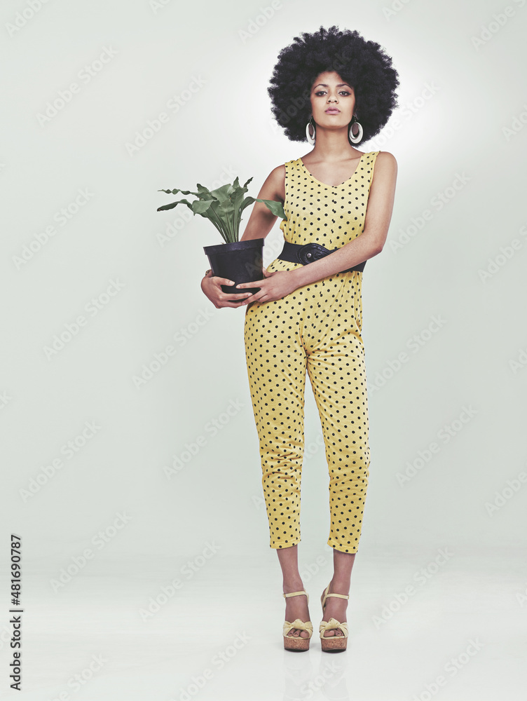 Shes got style...and a plant.. Full length portrait of young woman wearing a 70s retro jumpsuit hol