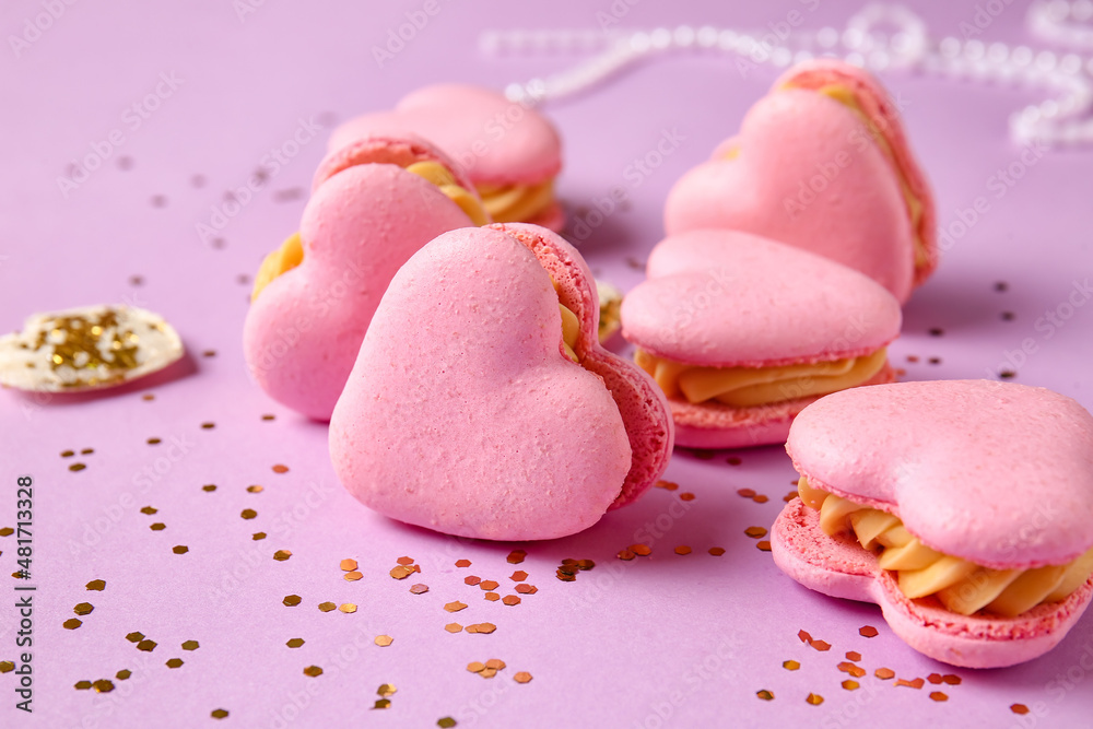 Tasty heart-shaped macaroons an confetti on purple background, closeup