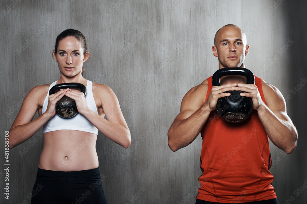 Theyre committed to staying in shape. A man and woman working out with kettle bells at the gym.