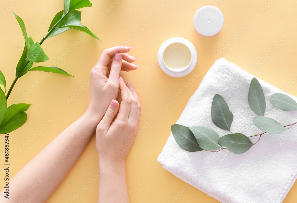 Female hands with jar of cosmetic cream and bath towel on color background