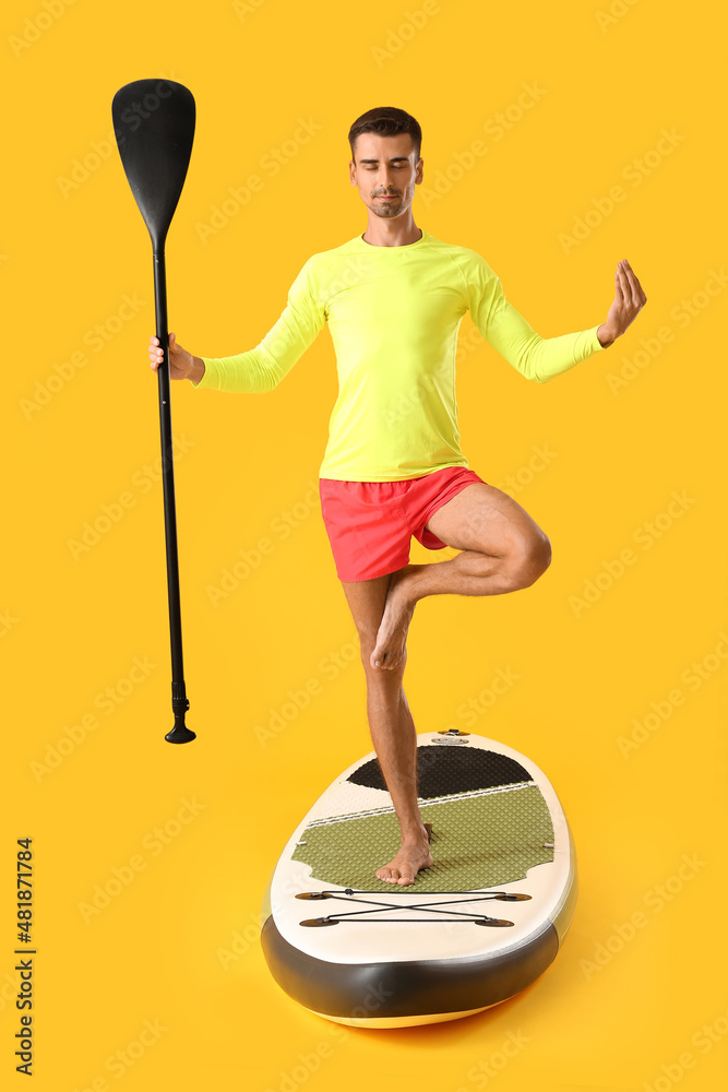 Young man meditating on sup board against color background