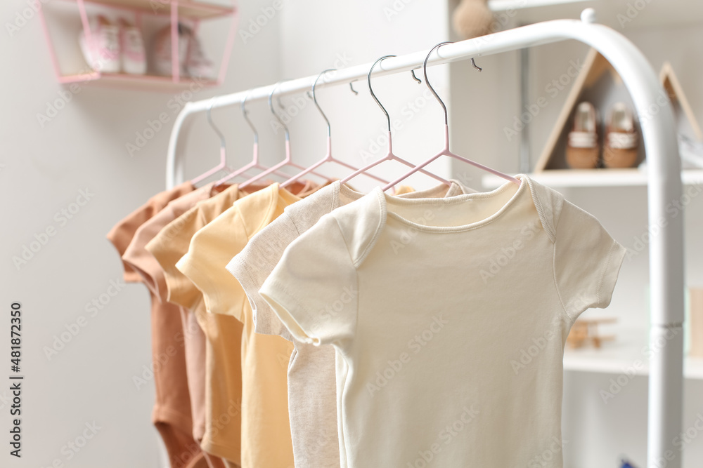 Rack with baby bodysuits in light childrens room, closeup