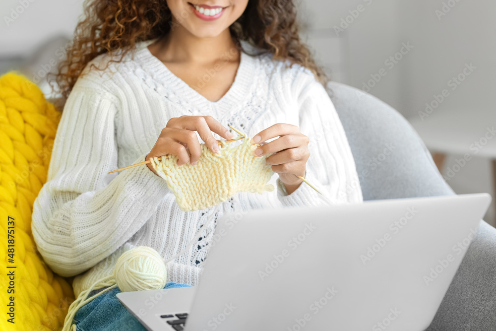 Young African-American woman taking online knitting classes at home