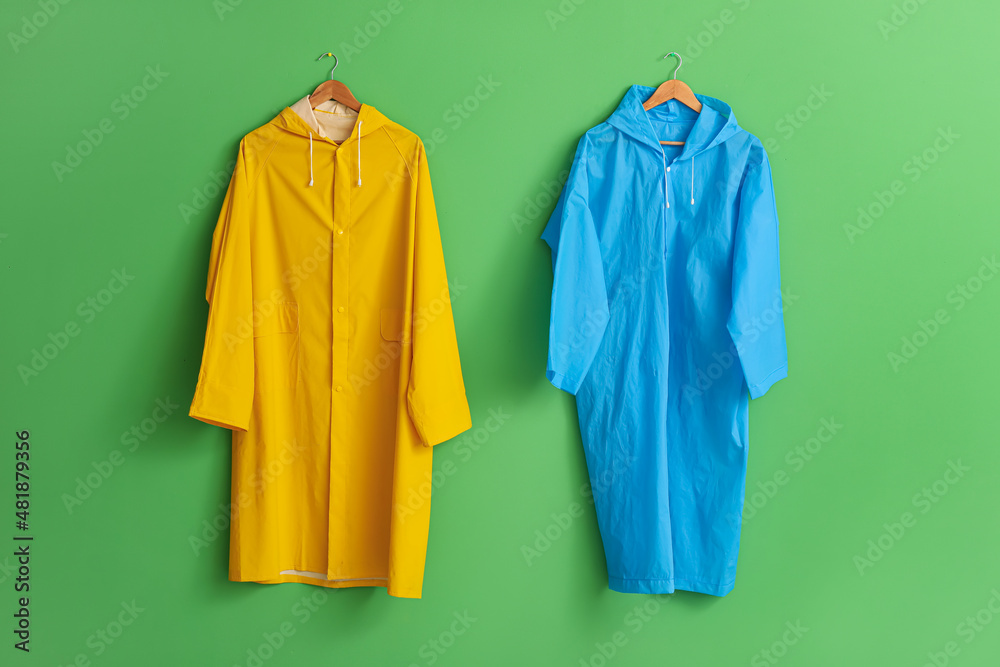 Bright raincoats hanging on green wall