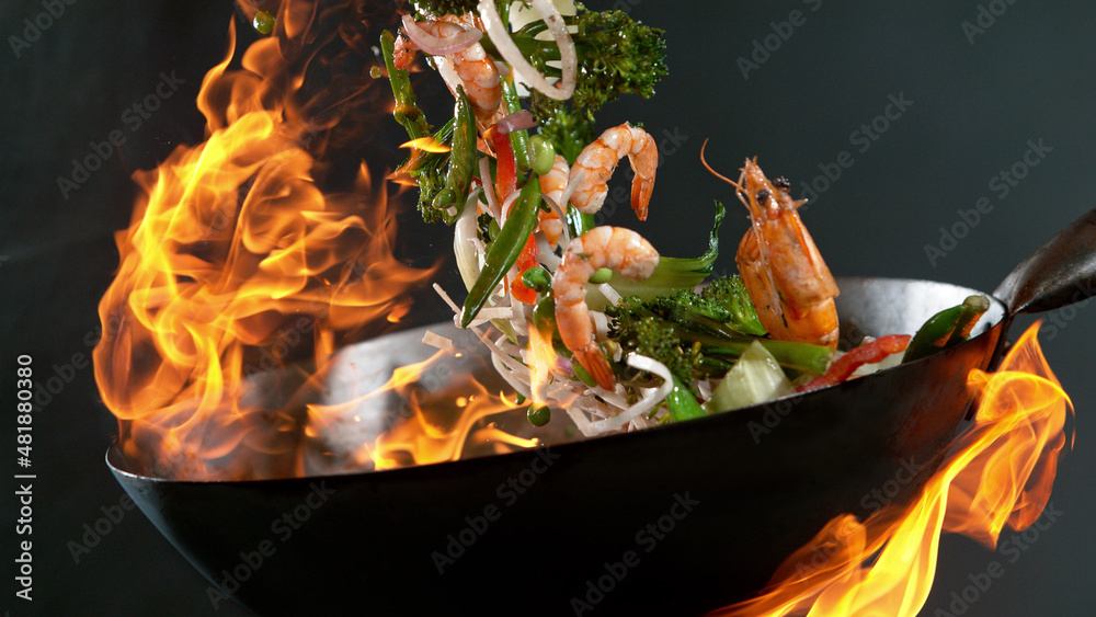 Closeup of chef throwing prawns from wok pan in fire.