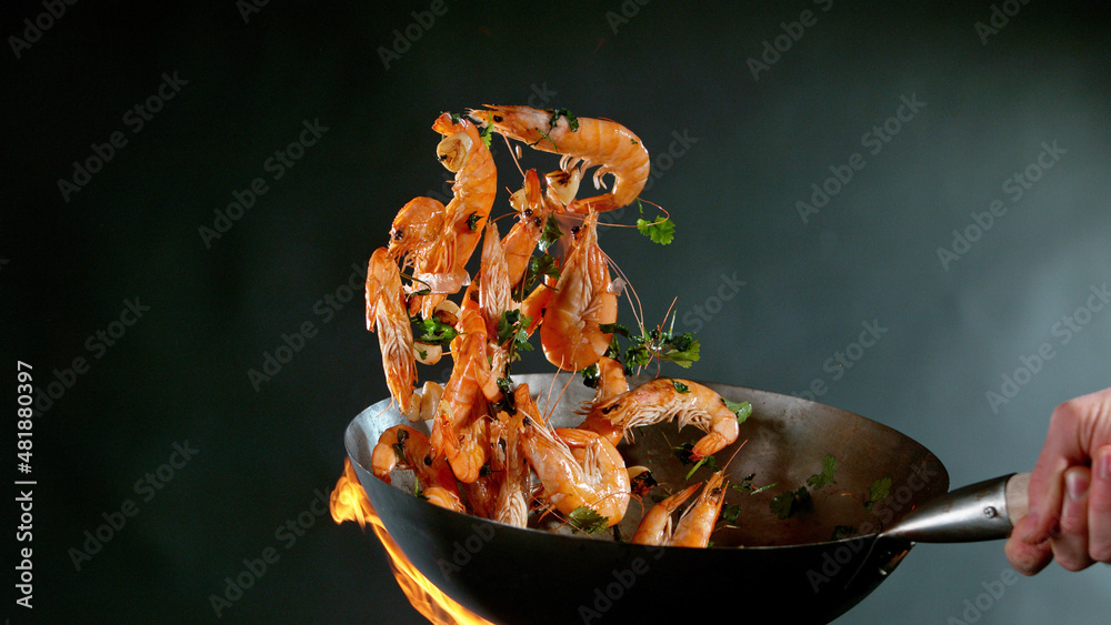 Closeup of chef throwing prawns from wok pan in fire.