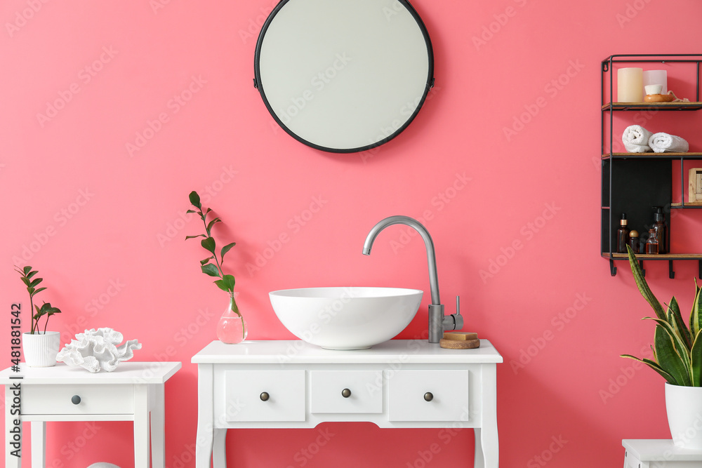 Interior of stylish bathroom with sink, mirror and pink wall