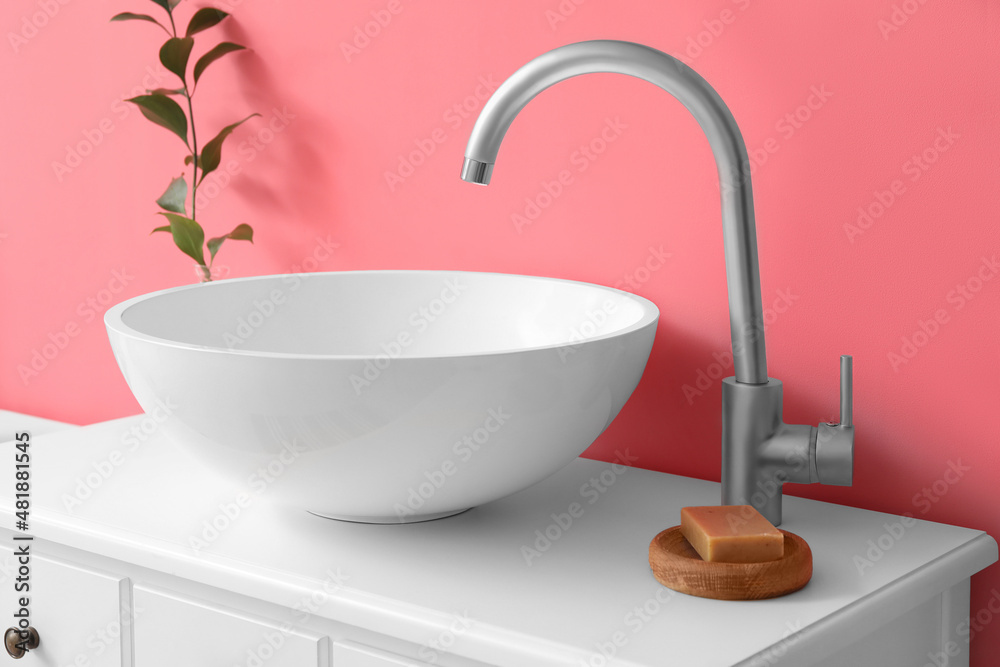 Table with sink, soap and plant branch in vase near pink wall