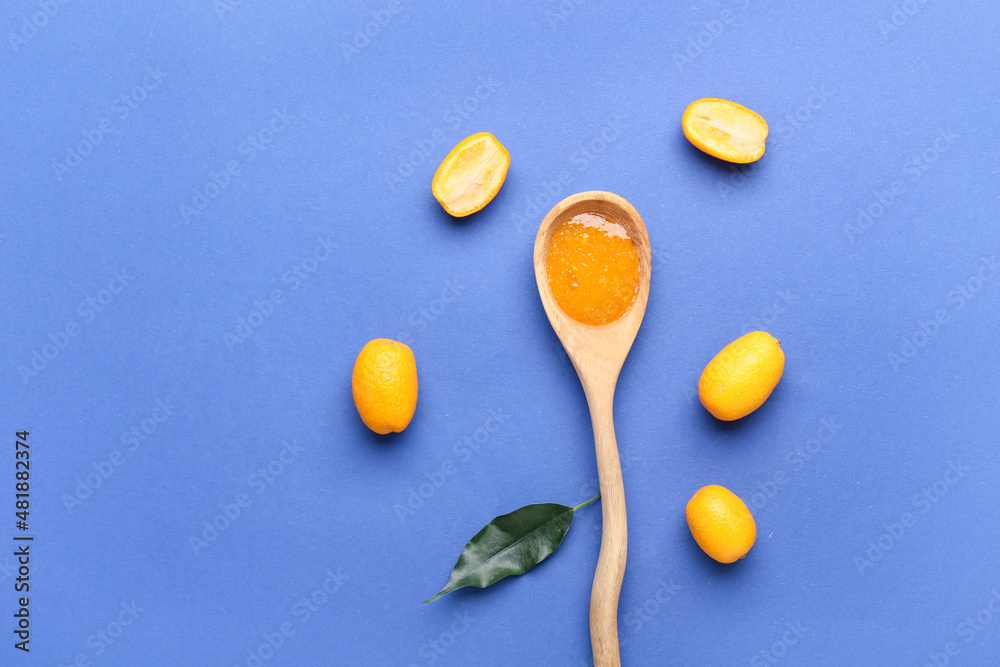 Spoon of tasty kumquat jam and fresh fruits on blue background