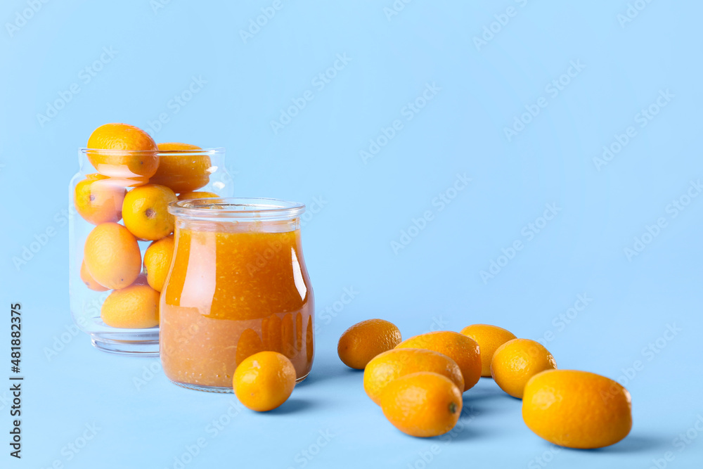 Jar of tasty kumquat jam and fresh fruits on blue background