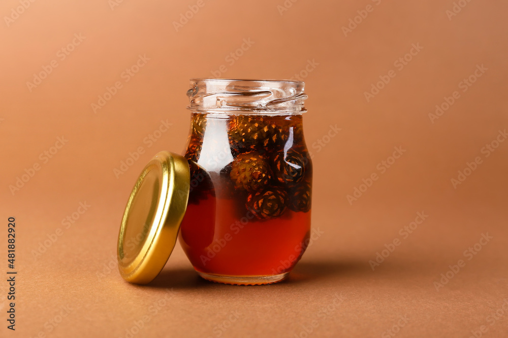 Jar of tasty pine cone jam on color background