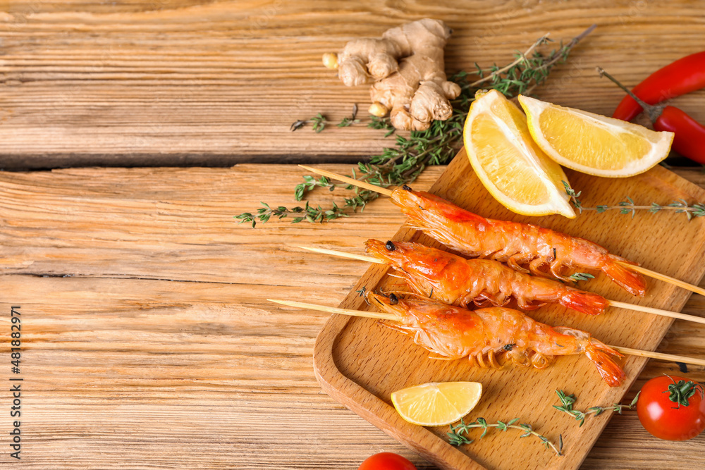 Board with grilled shrimp skewers on wooden background